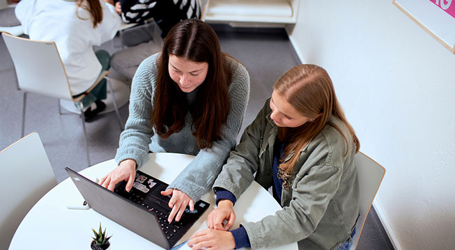 To jenter som sitter foran en pc og jobber