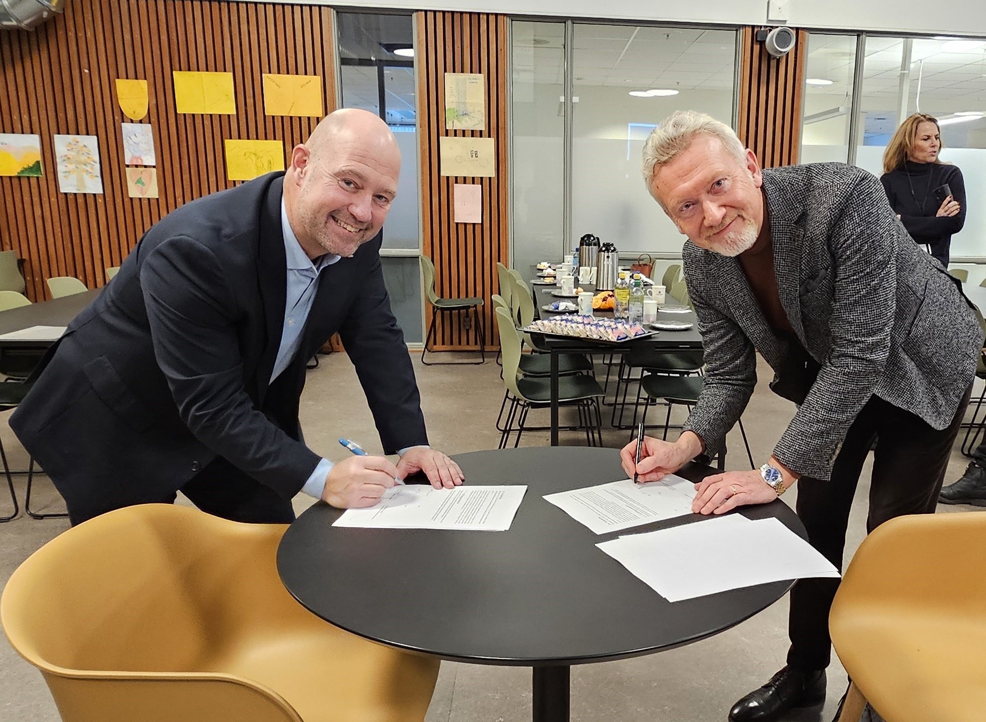 To menn som signerer på to ark som ligger på et bord. Foto