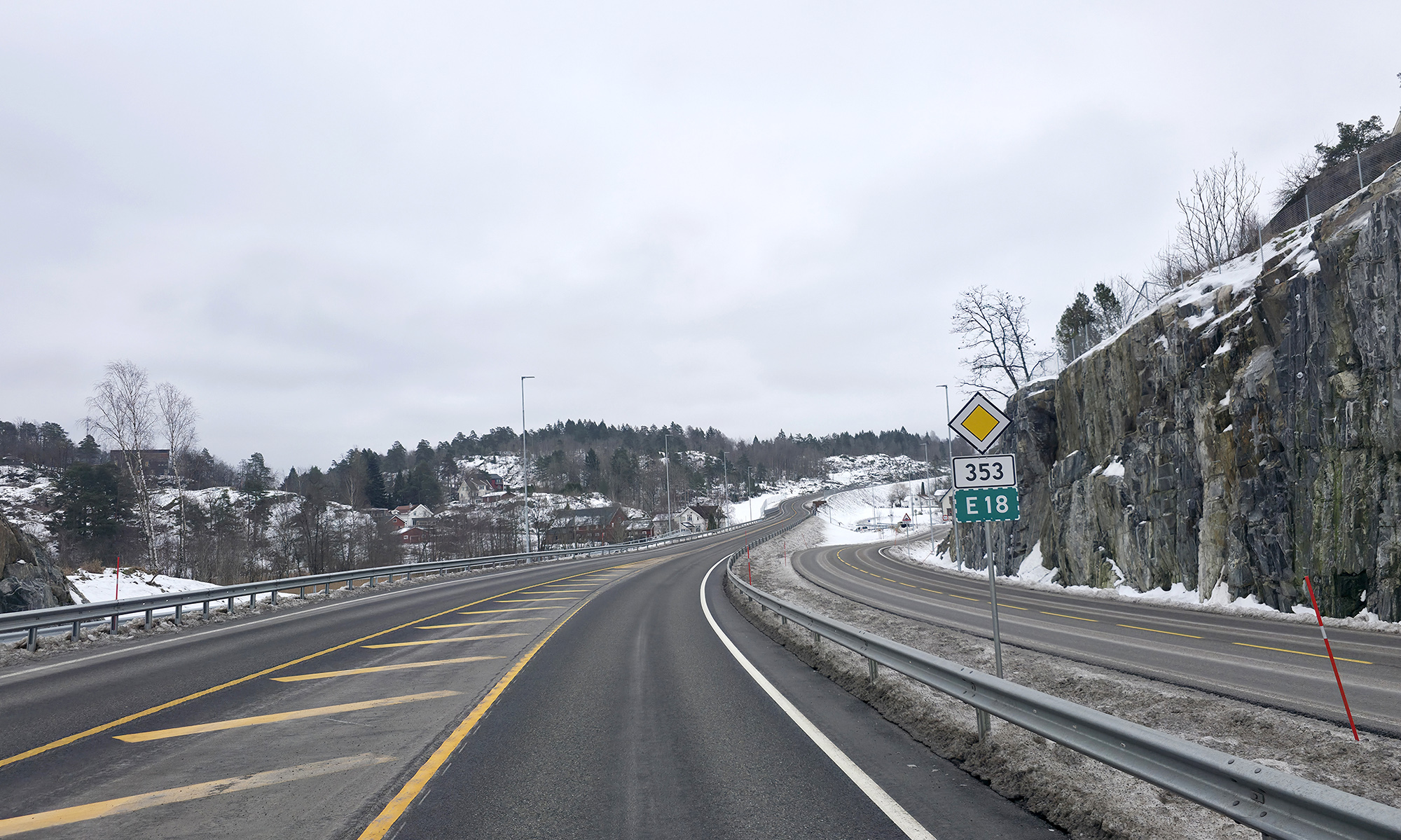 Viser smal vei på Rugtvedt, med uoversiktlig kryss inn fra høyre. Trailer kjører mot betrakteren av bilde. I bildets bakkant ser man bebyggelsen i området.