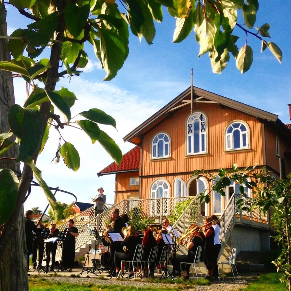 Et symfoniorkester spiller foran et gult sveitserhus.