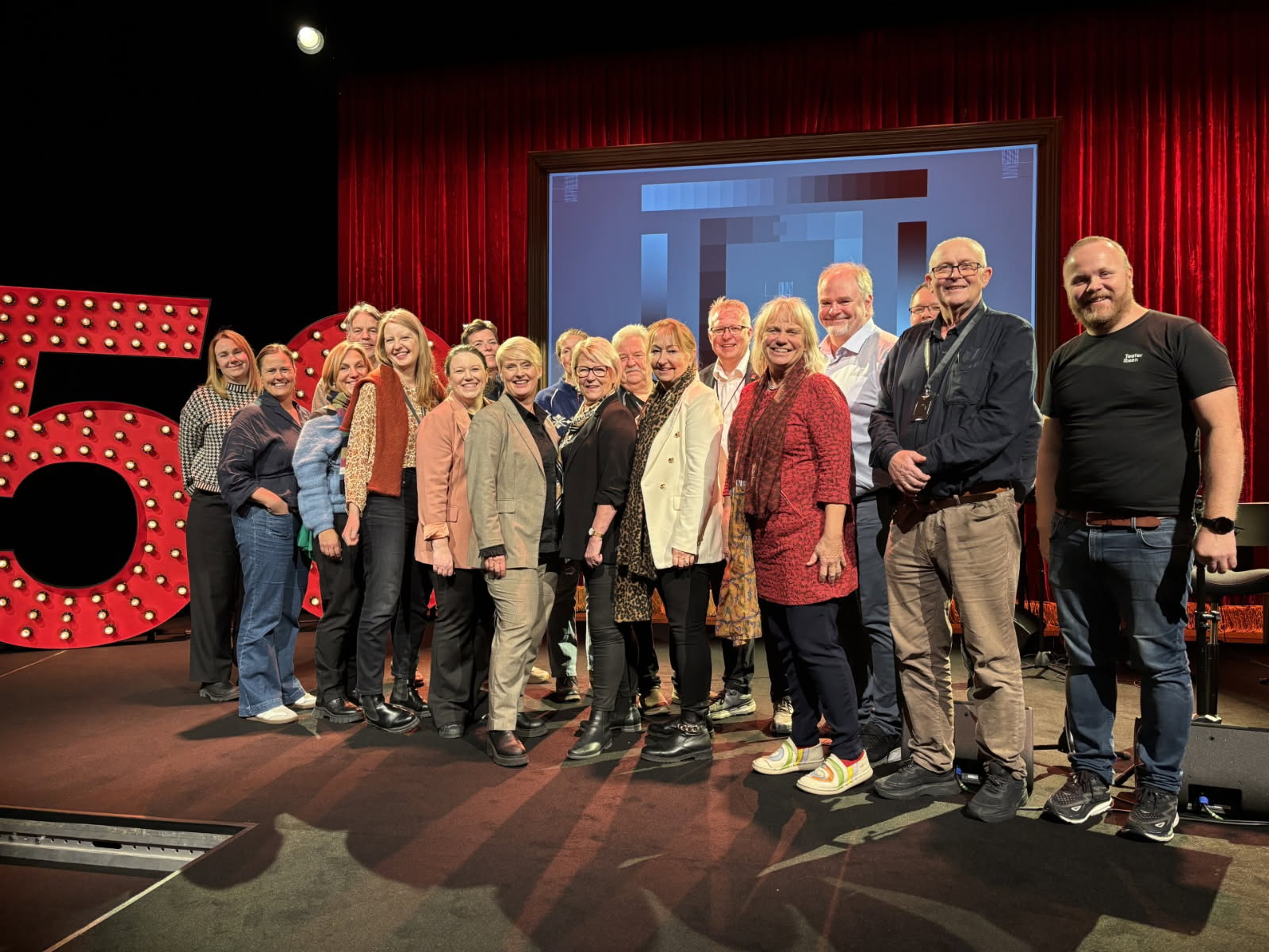 Mange folk står på en scene, de er fylkespolitikere på besøk hos Teater Ibsen.