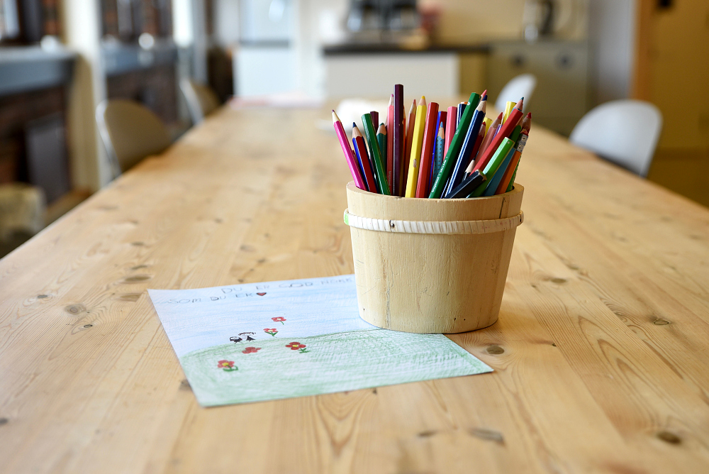 Bord med et ark med tegninger og en boks med tegnestifter.