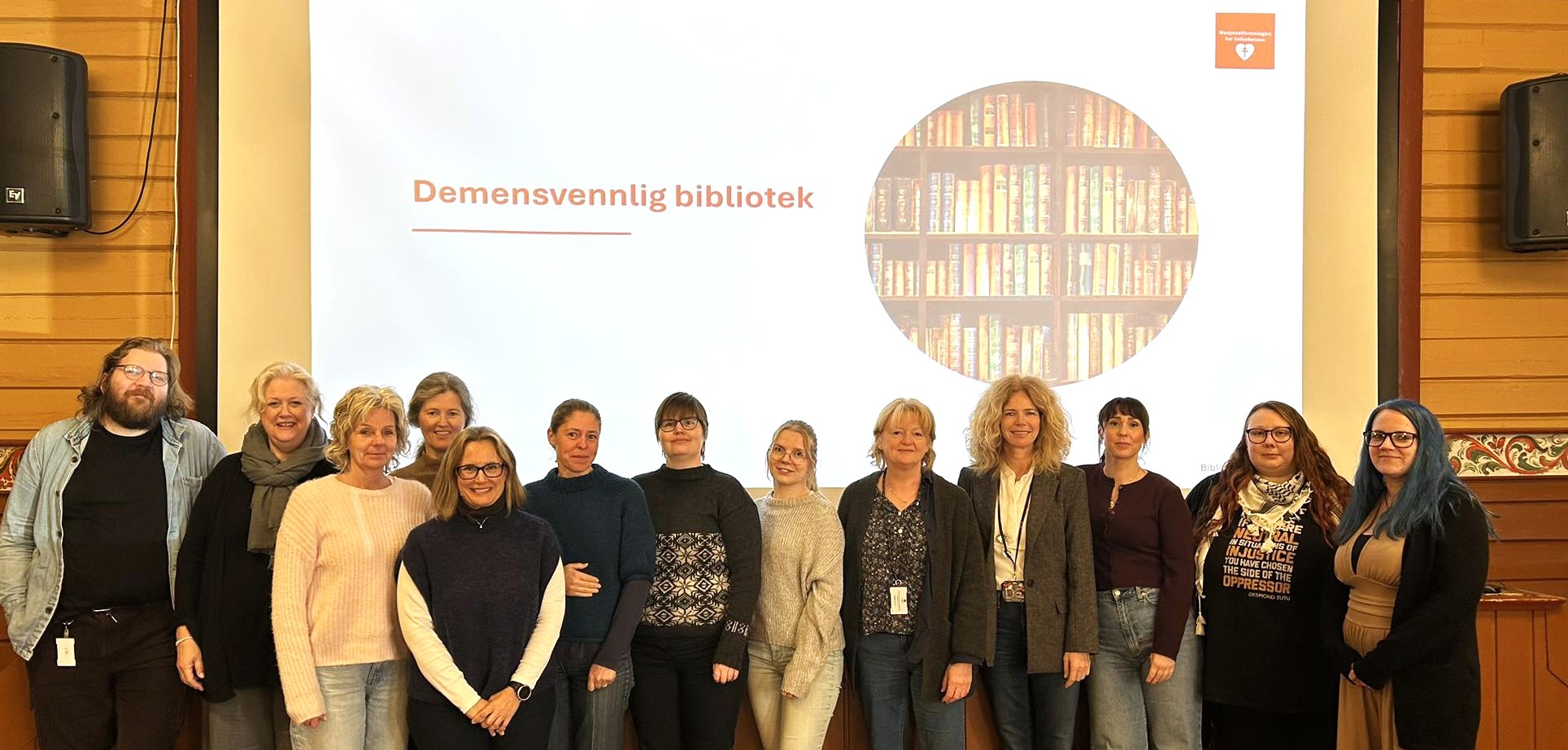Flere mennesker står oppstilt foran et bilde som forteller at de er demensvennelig bibliotek.