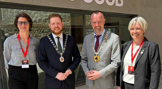 To kvinner og to menn ser inn i kamera og smiler. Alle er pent antrukket i dress eller drakt. Mennene i midten av bildet av ordførerkjeder rundt halsen.