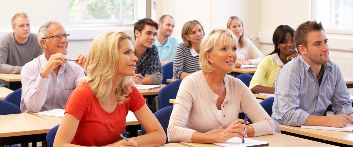 Voksne mennesker sitter ved pulter i et klasserom.